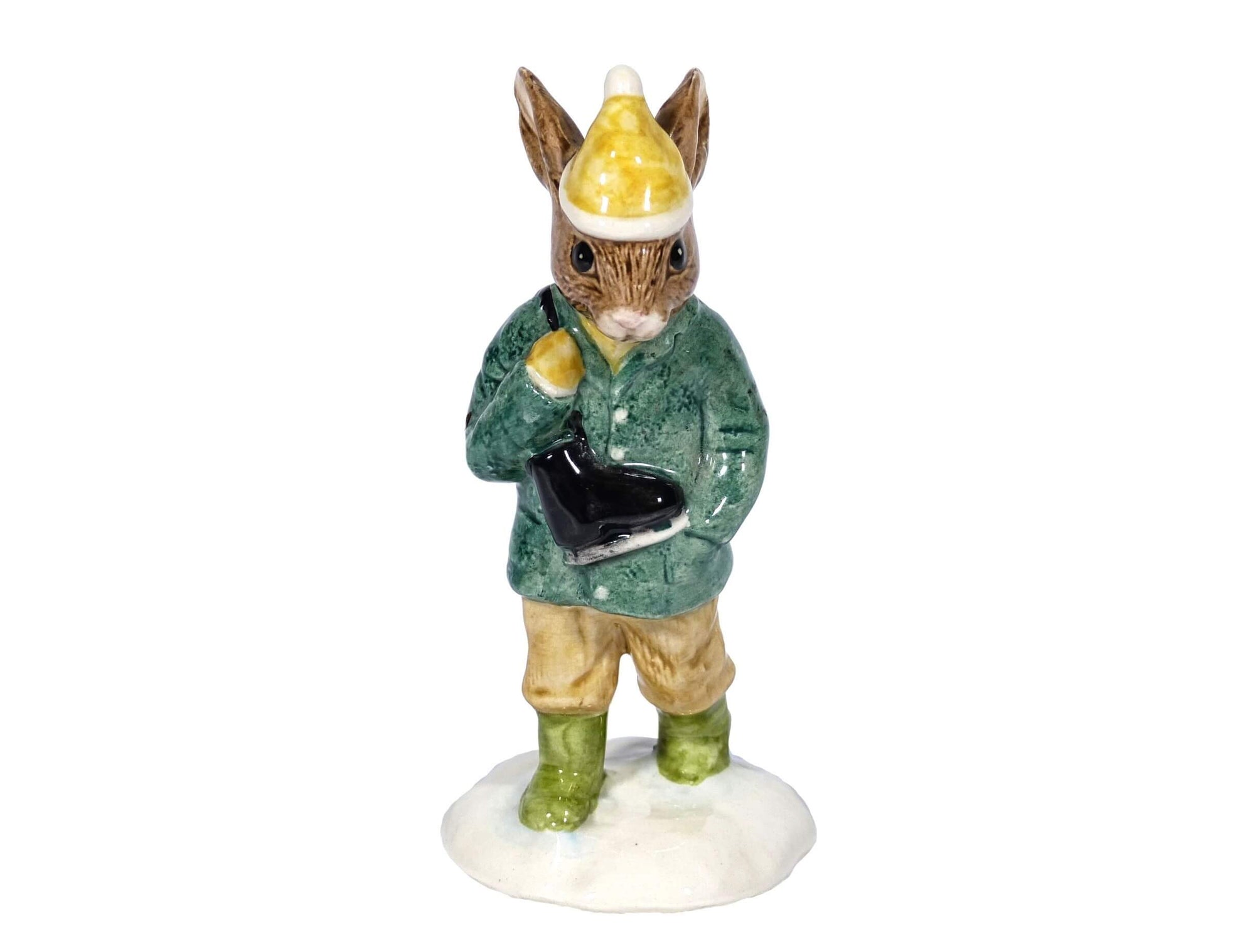 The bunny is wearing a green coat, a yellow hat with a white pompom and green boots. His black skates are hanging over his shoulder.