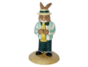 The bunny is wearing an aqua and white striped jacket, green trousers and bow tie and a yellow hat with a green stripe. He is playing his yellow trumpet.